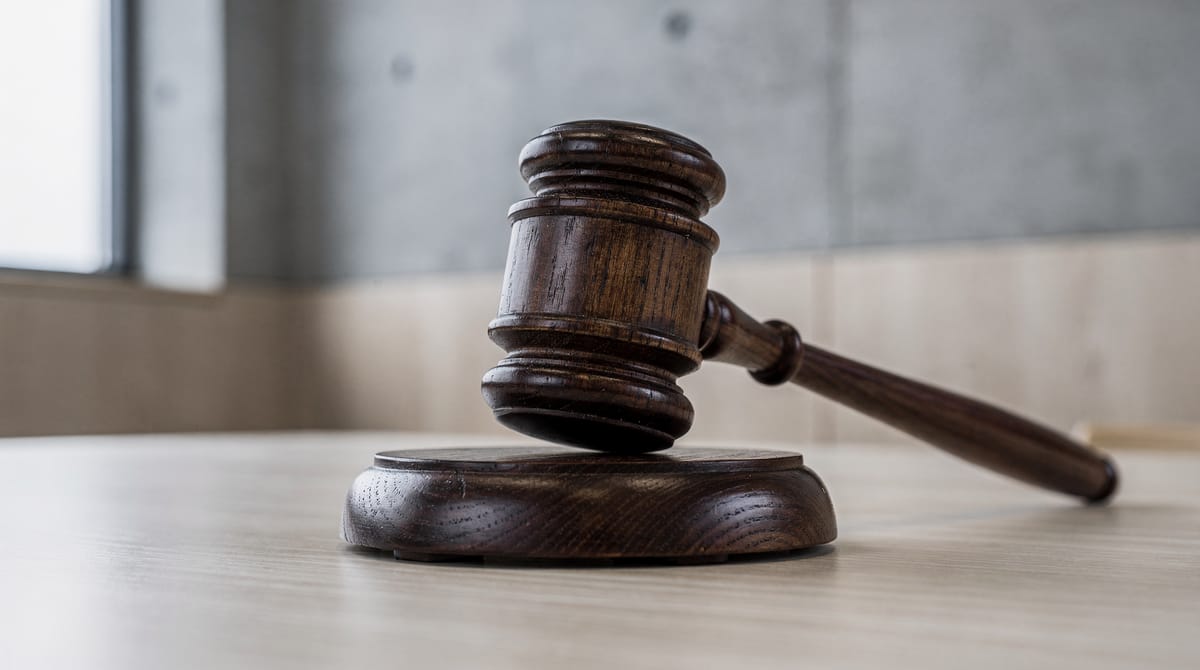 Close-up of a wooden gavel resting on a sound block in a modern, minimalist Scandinavian courtroom. The depth of field is shallow, focusing sharply on the wood grain of the gavel, symbolizing the finality and importance of the rule of law. Cold, natural light coming from a side window.