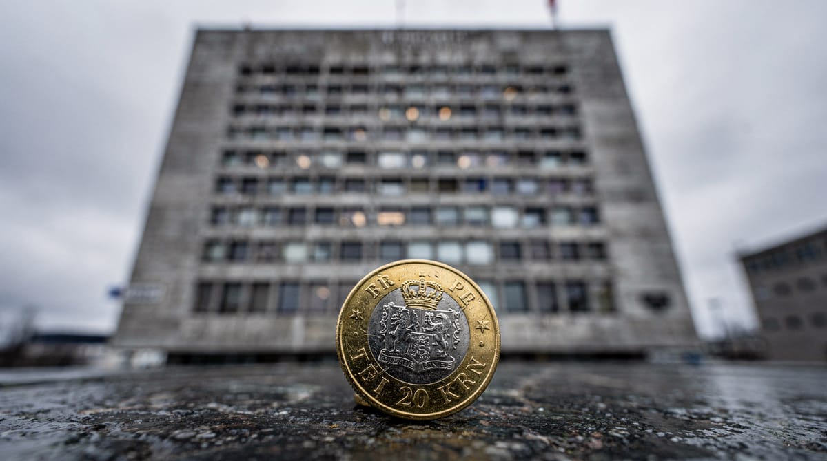 A brutalist, imposing government building architecture in Oslo, shot from a low angle to make it look looming and disconnected from the ground level. The sky is overcast and grey. In the foreground, a single, sharp focus on a calculator or a coin, symbolizing the economic cost to the individual taxpayer verses the massive machinery of the state. Style: Cold, desaturated tones, symbolizing bureaucracy.