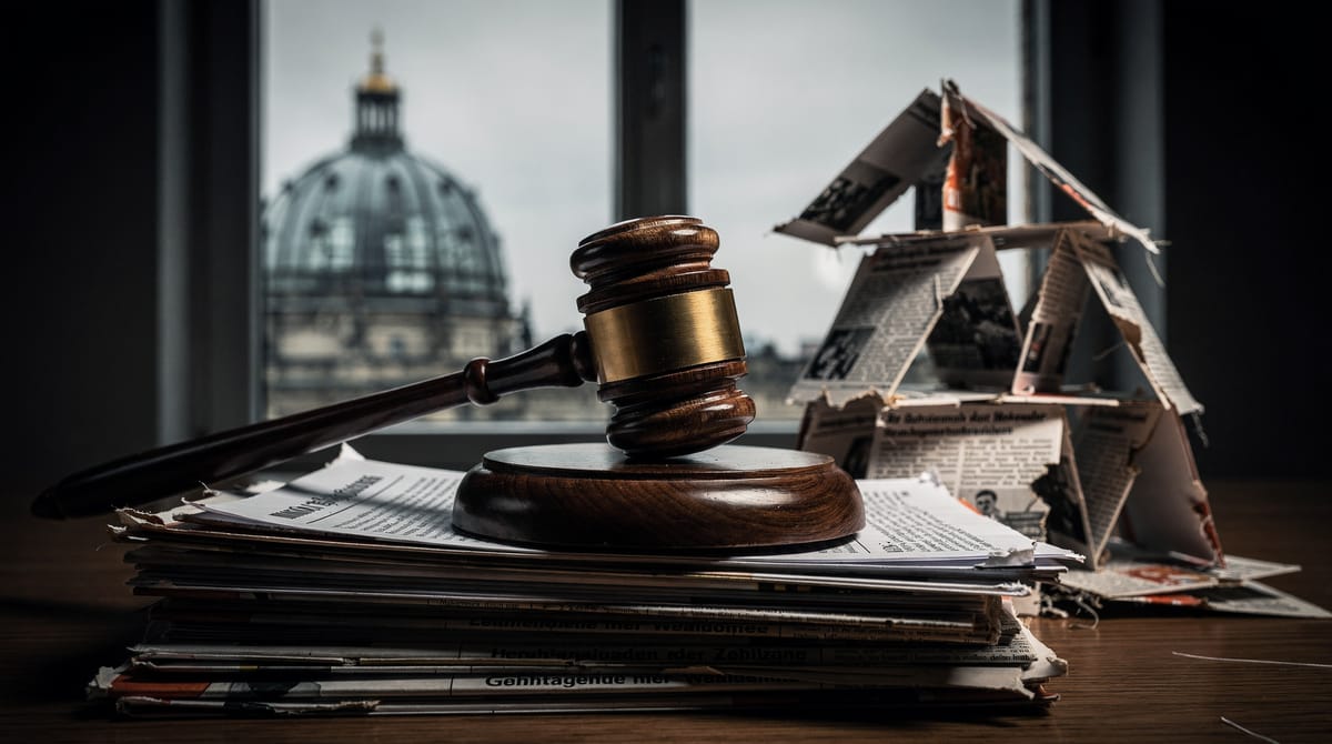 Symbolic image of a collapsing house of cards made of newspapers. One card clearly shows a blurred headline reminiscent of 'Correctiv' or 'Secret Plan', crumbling down. In the background, a gavel (judge's hammer) rests on a table, signifying legal judgment overtaking media narratives. Sepia and grey tones, detailed depth of field.